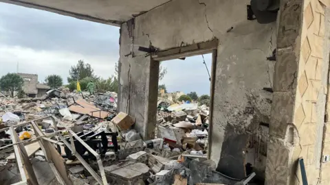 Debris of the house by a remaining wall with a doorway in it